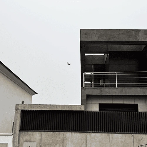 Vista del exterior de un edificio de diseño moderno en construcción. La estructura combina hormigón visto y grandes bloques de color negro. En el primer plano, hay una valla de hormigón con lamas metálicas verticales negras.