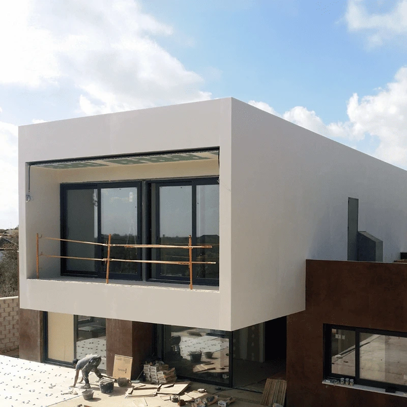 Detalle de fachada de lujo combinando grandes formatos de piedra oscura, travertino y estructuras blancas geométricas en obra de construcción integral.