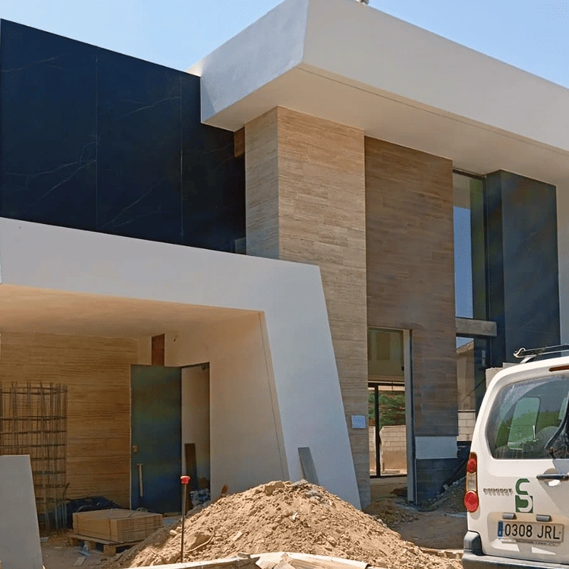 Construcción de vivienda de diseño con gran voladizo superior y planta baja revestida en piedra tecnológica marrón, obra nueva a precio cerrado.