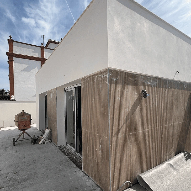 Ejecución de fachada moderna en vivienda unifamiliar con revestimiento de paneles porcelánicos imitación madera y acabados en blanco minimalista.