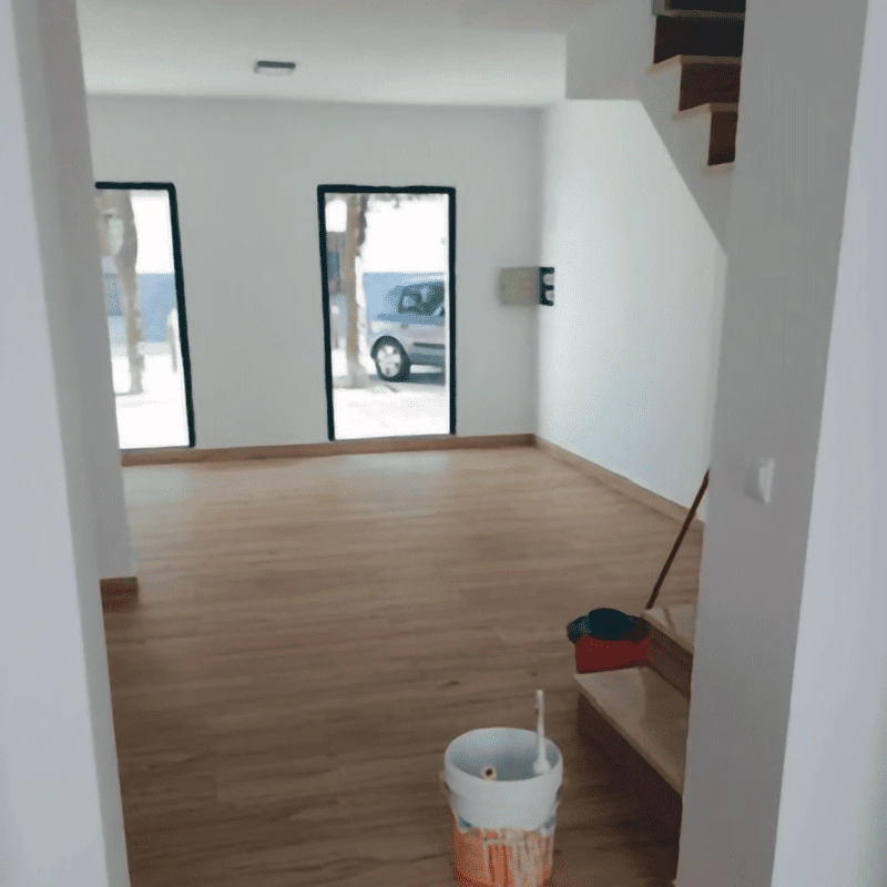 Salón diáfano con iluminación natural y escalera de madera, mostrando la instalación de pavimentos laminados de alta calidad en reforma de vivienda.
